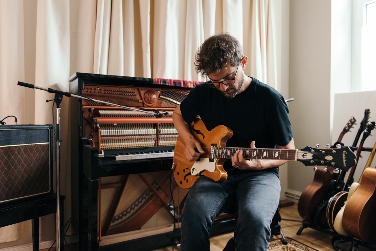 Claudio Donzelli playing electric guitar in front of an open upright piano in a bright room