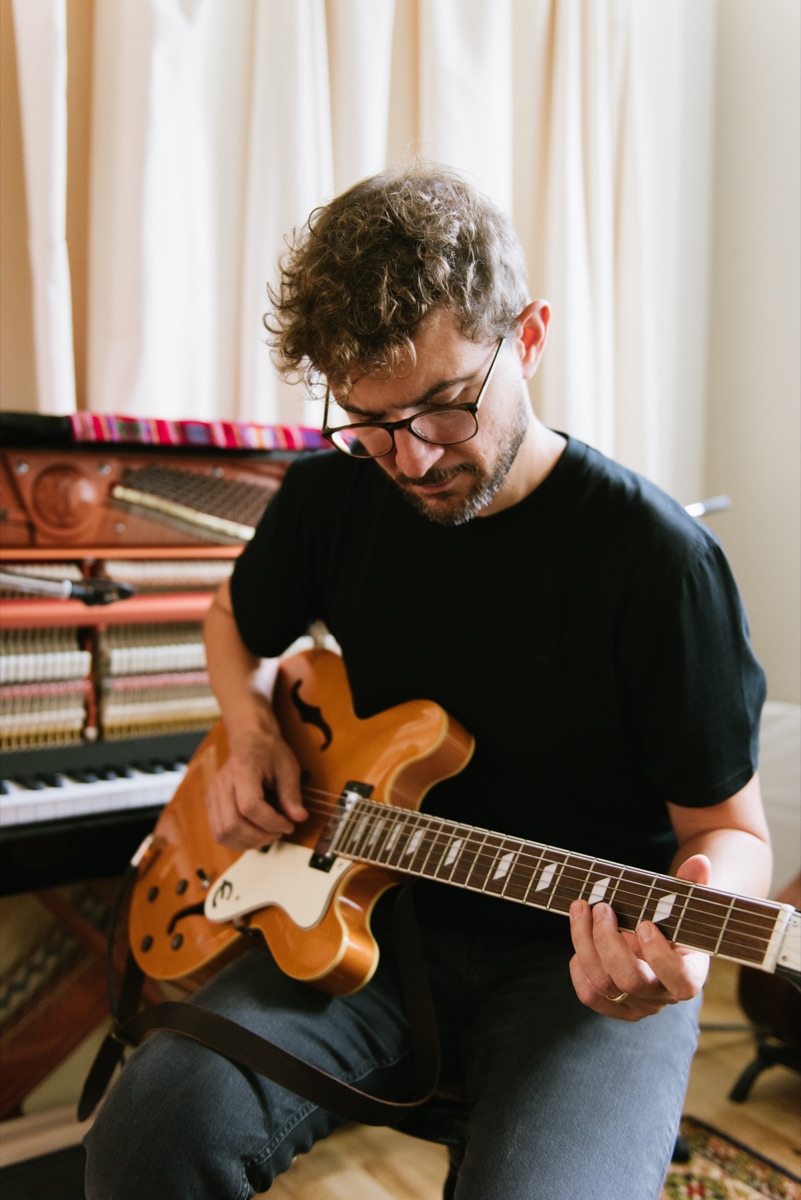 Claudio Donzelli playing a hollow-body electric guitar, looking down at the strings