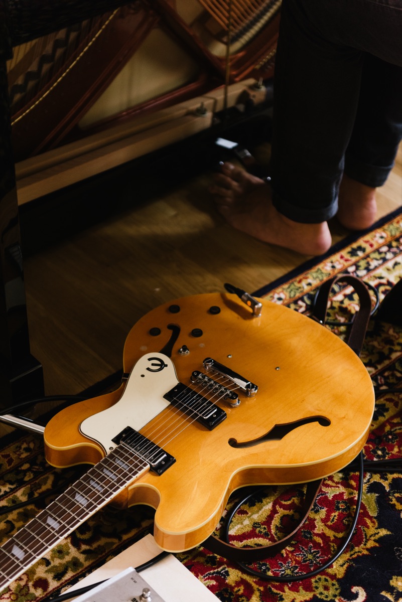 A hollow-body electric guitar lying on a patterned rug, bare feet in the background