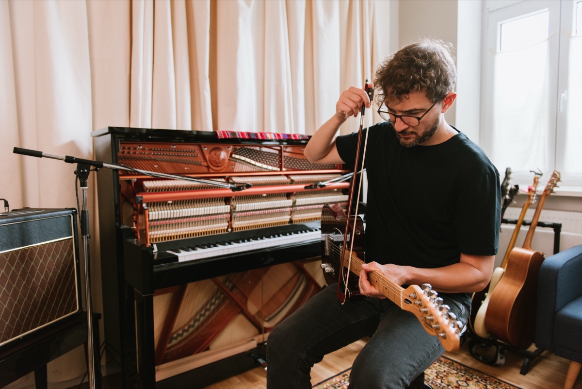Claudio Donzelli playing an electric guitar with a violin bow in his studio