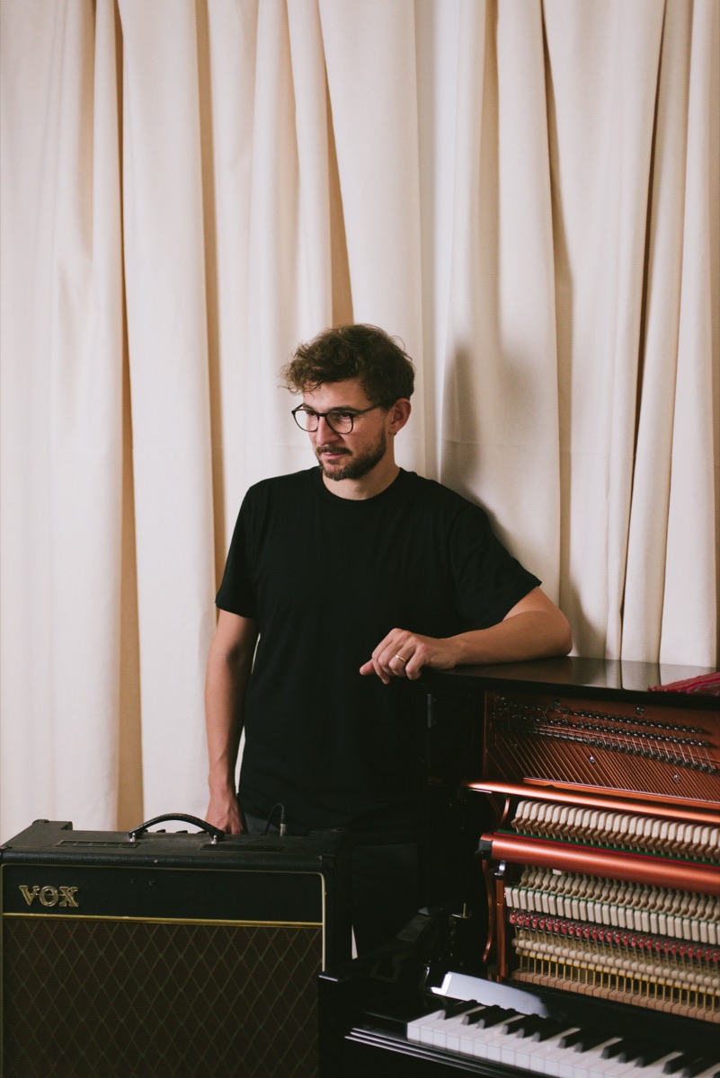 Claudio Donzelli standing beside a Vox amplifier and an upright piano